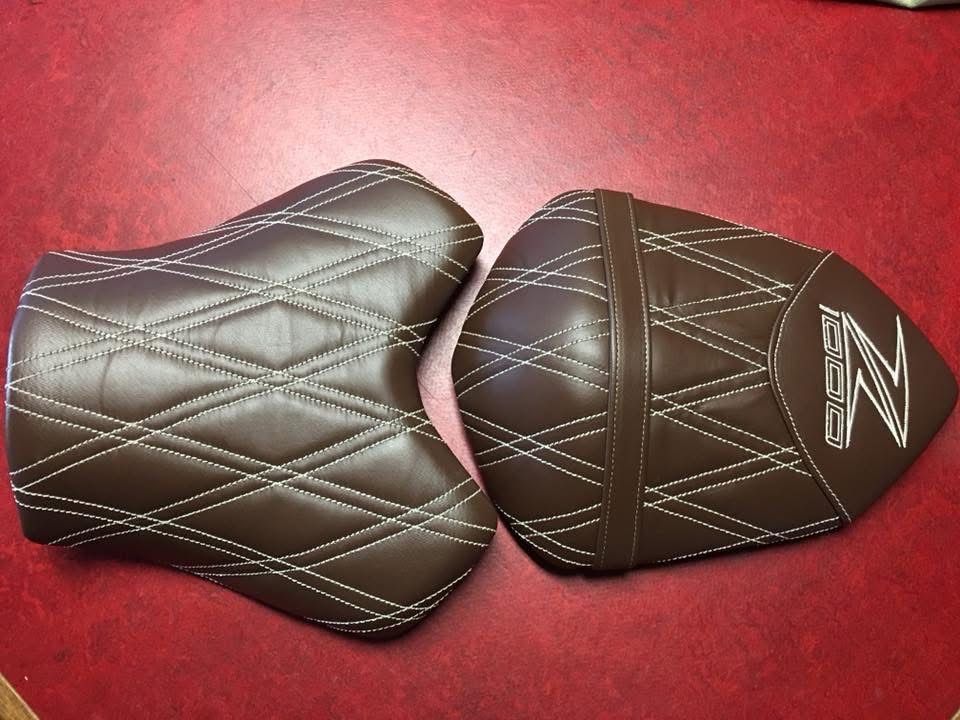 Twee buddyseats in bruin leer met ruitstiksel en een geborduurd logo